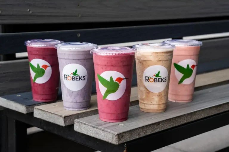 Five colorful Robeks smoothies lined up on an outdoor bench